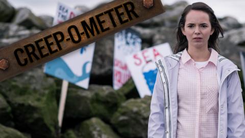 A girl standing on a beach in front of a rocky hill with lots of protest signs against polluting the ocean.