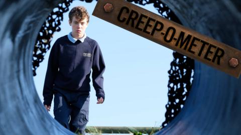 A boy in uniform outside looks through a dark tunnel he doesn't want to go down.