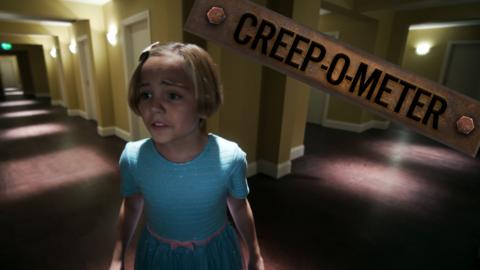 A girl looks scared as she stands in a hotel corridor stretching out in both directions with no end.