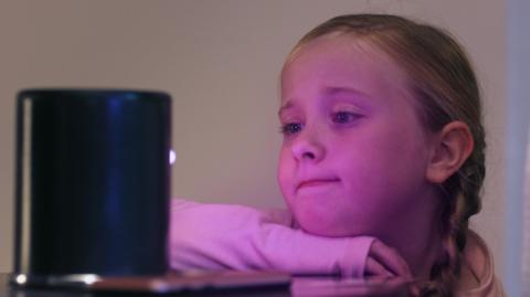 A girl looking at a black box emitting a pink light.