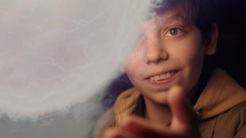 A boy smiling as he reaches for a glowing orb.