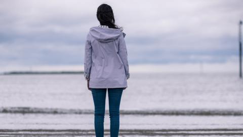 A girl standing on a beach looking out to the sea from the beach.