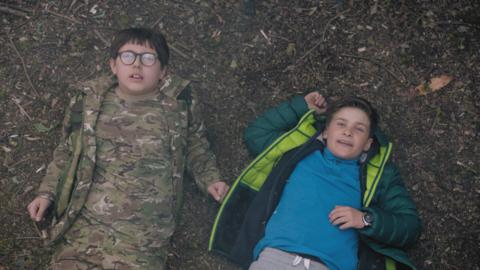 Two boys lying down in the woods.