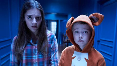 A teen girl and young boy stand in a blue corridor looking frightened.