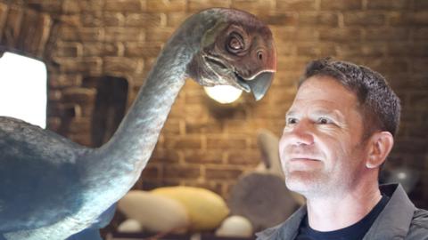 Steve Backshall looking at a dinosaur.