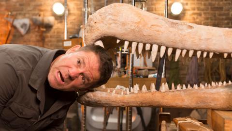 Steve with his head in the jaws of a model dinosaur.