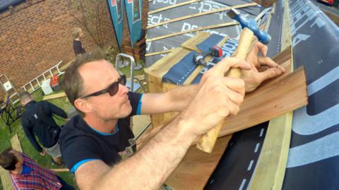 A man hammering tiles onto a roof.