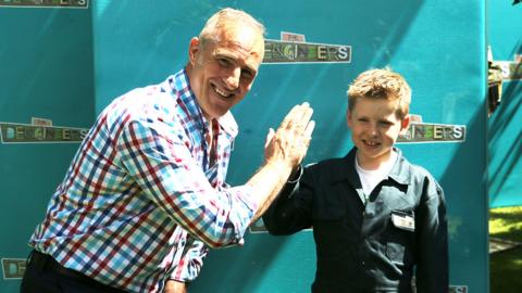 A boy and a man give each other a high-five as they are building a den with the Dengineers.