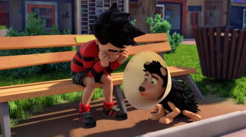 Dennis and Gnasher sat looking upset, and Gnasher has a cone on his head.