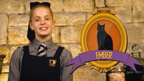 A girl in a school's uniform next to a framed picture of a black cat called Ember.