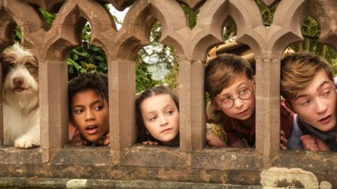 Timmy, George, Anne, Dick and Julian peer through the gaps of an old wall.