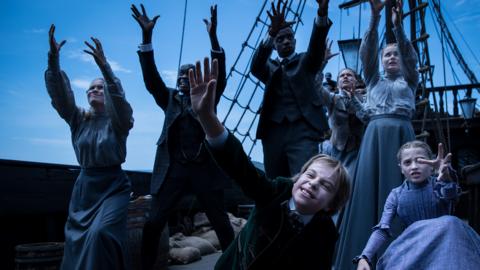 A group of vampires on a ship raising their arms up.