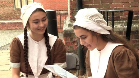 Ava and Polly, who play Harriet and Sheila, in a brick courtyard.