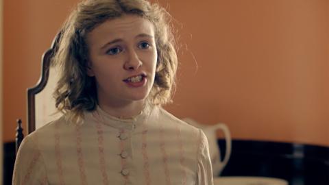 A girl with short curly blonde hair looking angry in a white frilly dress, Emily.