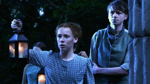 A group of children in a wood at night looking into the distance.