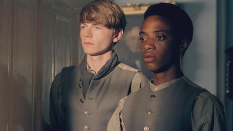 Two young boys in Victorian clothes looking worried in an office doorway.