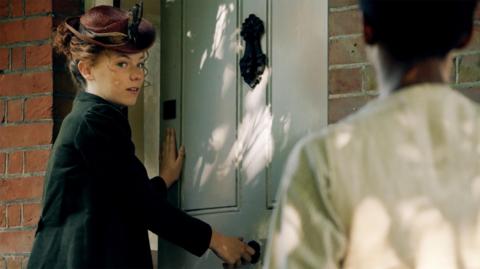 A girl opening a door to an old cottage.