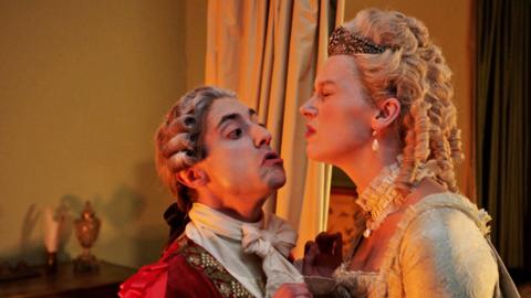 Cast members of Horrible Histories dressed as Louis XVI and Marie Antoinette pretending to kiss one another.