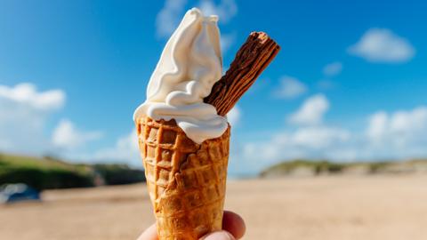 A cone of ice cream with a flake. Beach in background.