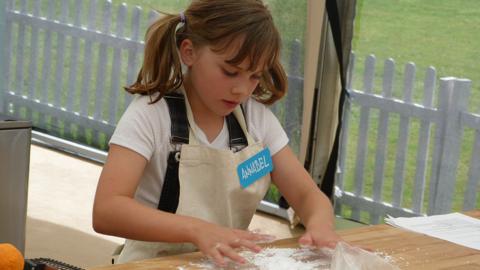 A girl is standing at a counter covering the surface with flour ready for baking.