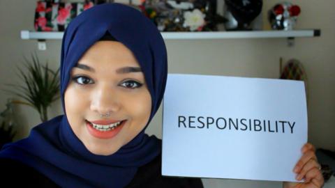 A young lady holding up a piece of paper with responsibility written on it.