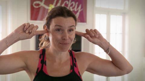 A woman with brown hair puts her fingers in her ears.