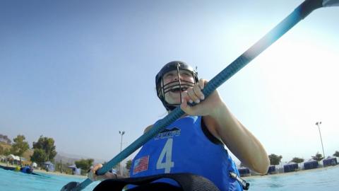 A girl laughs while sitting in a kayak holding a paddle.