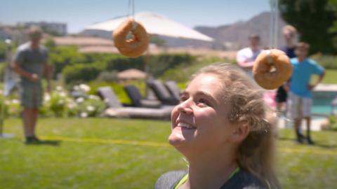 Tilly reaches up to eat a donut from a string.