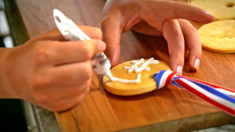 Tilly decorates a biscuit medal '#1' in white icing.