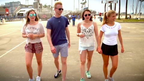 Three girls and a boy walk together on Venice Beach in sunny clothing.