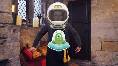 A girl dressed as a witch, with an astronaut helmet superimposed on her head and a cartoon alien flying in front of her. Maud from The Worst Witch.