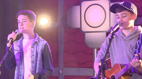 Two boys singing a cover song, one with a microphone while the other plays guitar, Max & Harvey.