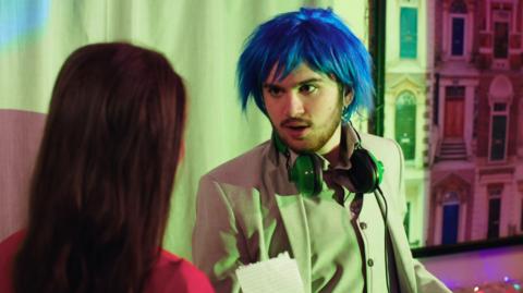 A guy in a blue wig with headphones around his neck.