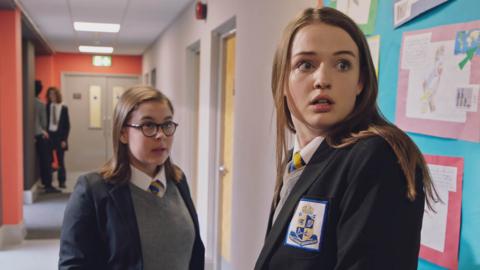 Lauren in a school corridor looking over her shoulder and looking scared.