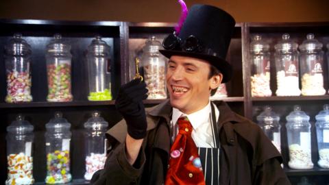 Ed dressed as a malevolent looking Victorian gentleman with bad teeth, holding a golden key.