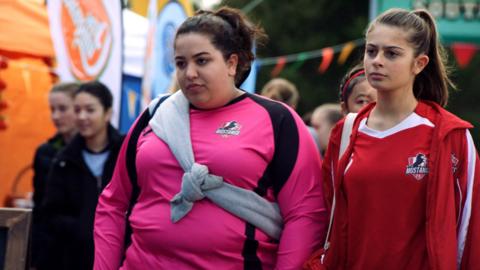 Two girls standing next to each other in football kit looking unimpressed. Liv and Marnie from Mustangs FC.