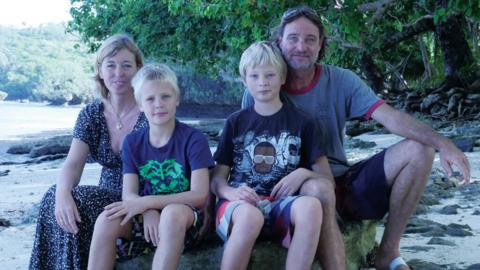 A man and woman sat on a beach with two boys.