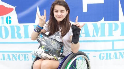 A girl in a wheelchair holding hr hands in the air.