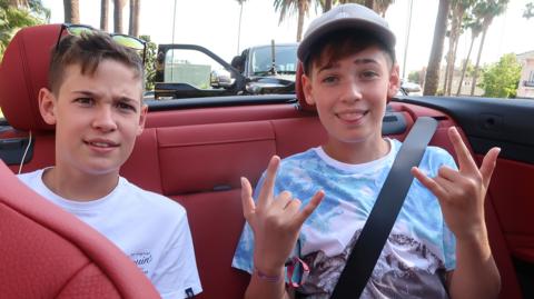 Two boys sat in the back of a sports car.