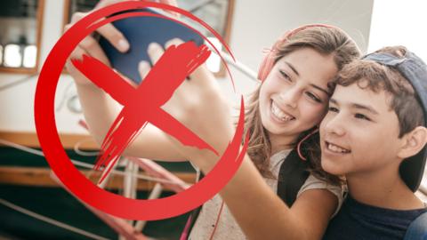 Two children taking a selfie with a red cross over the phone.