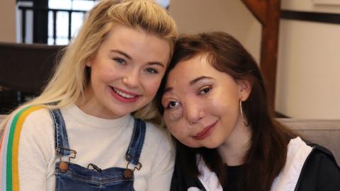 Two girls sat next to each other on a sofa smiling, Nikki Lilly and Georgine Toffolo.