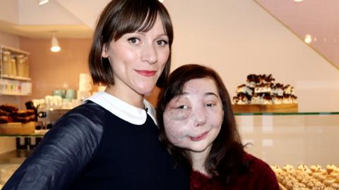 A woman and girl hugging and smiling at the camera in a cake shop.