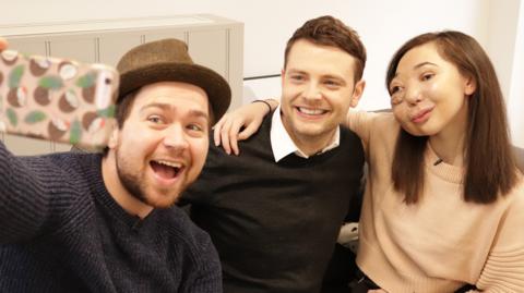 Two men taking a selfie with a girl on a sofa, Sam and Mark and Nikki Lilly.