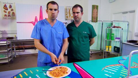 Dr Chris and Dr Xand are in their lab with a plate of spaghetti on the table.