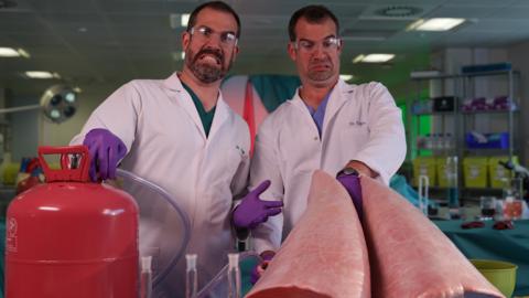 Two doctors inflating a set of cow lungs while looking shocked. Dr. Chris and Dr. Xand from Operation Ouch.