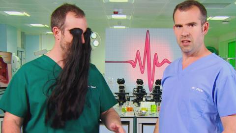 Two men wearing scrubs while one has long fake eyebrows going down his chest.