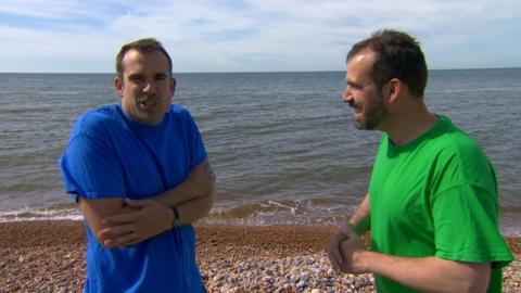 Two men standing in a beach, one looking cold and one looking warm. Dr. Chris and Dr Xand.