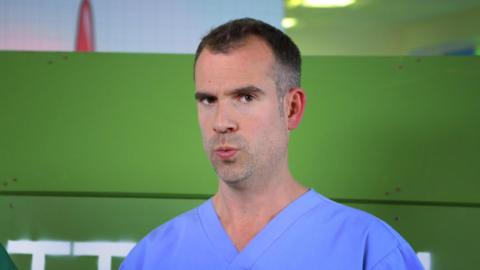 Dr Chris in blue scrubs looking confused in the lab.