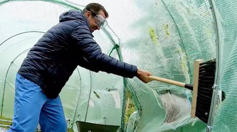 Dr Chris inside a huge green sheet tunnel, brushing the inside with a wooden brush.