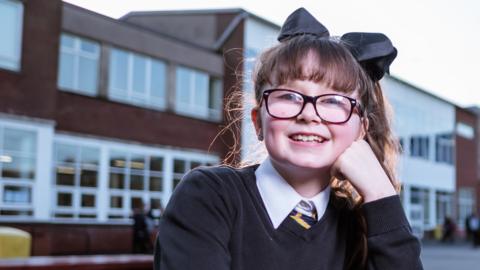 A schoolgirl leaning on her hand outside a school.